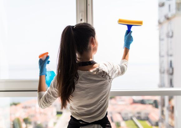 people, housework and housekeeping concept. Happy woman in gloves cleaning window with rag and cleanser spray at home Hemstädning